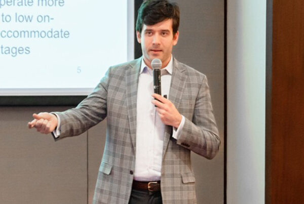 A man in a suit presents in front of a screen